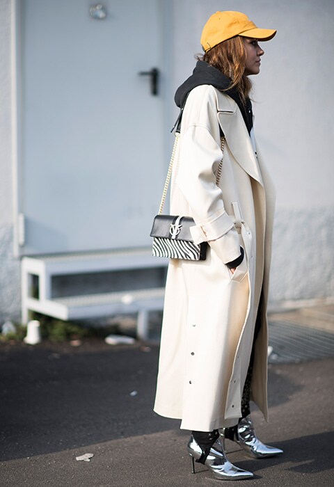 A fashion week attendee wearing a cropped hoodie and luxe trench coat, complete with silver boots.