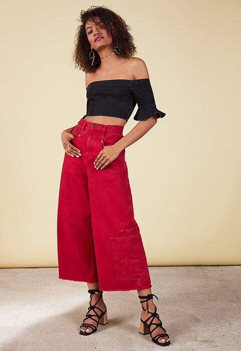 Model wearing black off-the-shoulder top with frill sleeve, red skater jeans and black lace-up sandals, all available at ASOS | ASOS Fashion & Beauty Feed