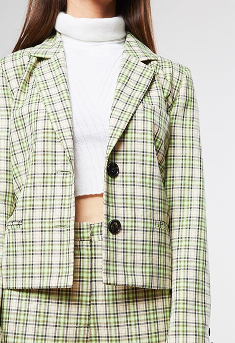 Celia wearing a green check blazer and white roll neck