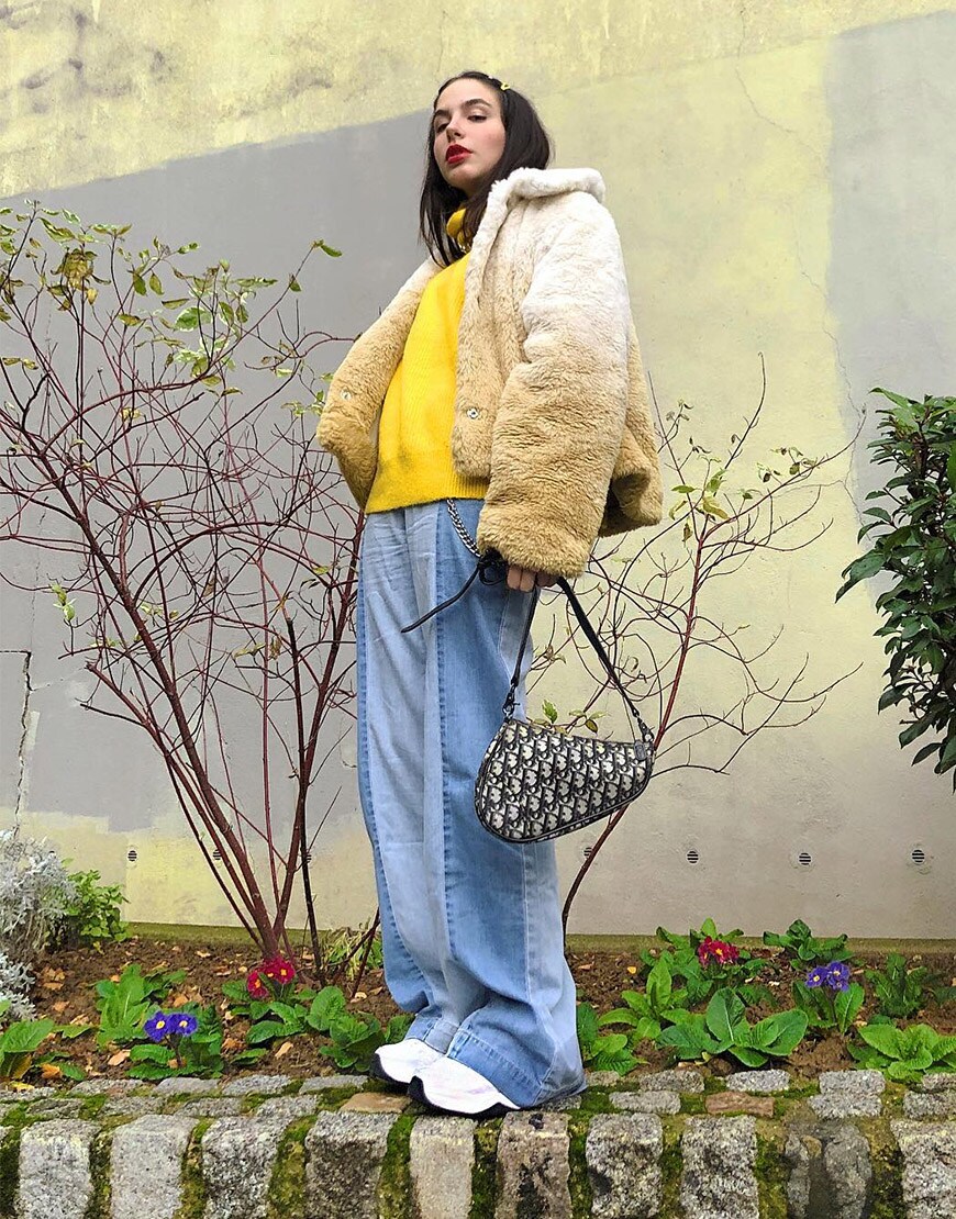 ASOS Barbara porte un pull jaune, un manteau en fausse fourrure, un jean et des baskets épaisses