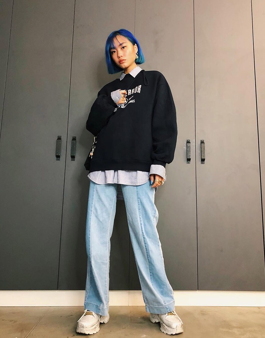ASOS Kicki porte un sweat-shirt avec une chemise sur un jean avec des grosses baskets