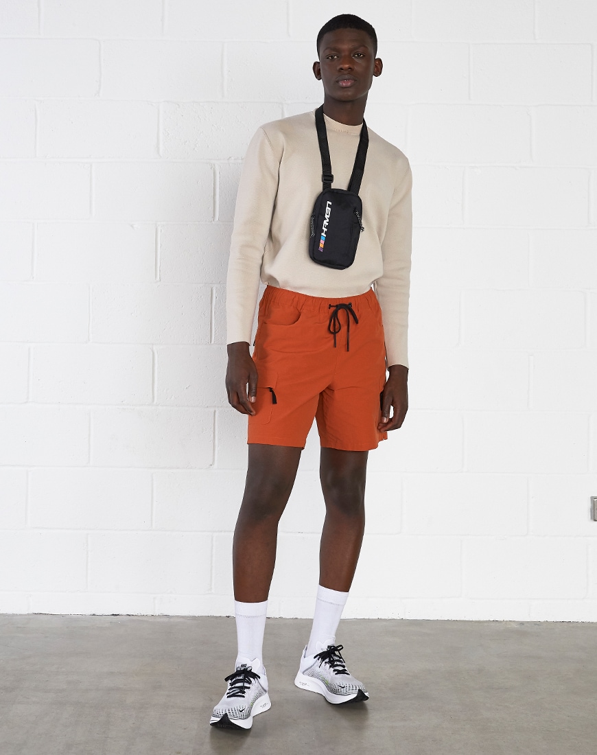 A model wearing a beige top, orange shorts and a flight bag | ASOS Style Feed