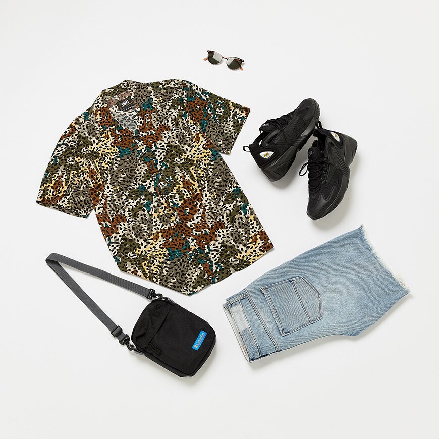 A flat lay image of a animal print shirt, ripped denim shorts, chunky trainers and a flight bag.