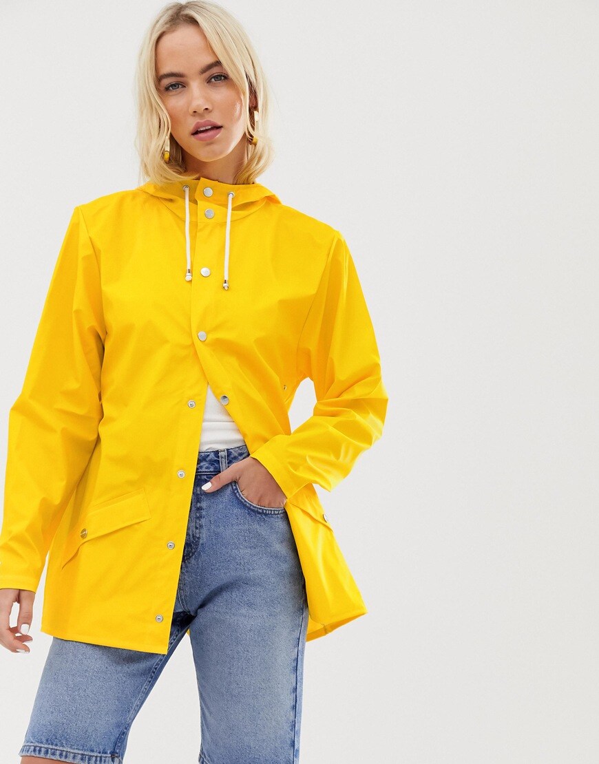 A picture of a model wearing a bright yellow waterproof jacket by Rains. Available at ASOS.