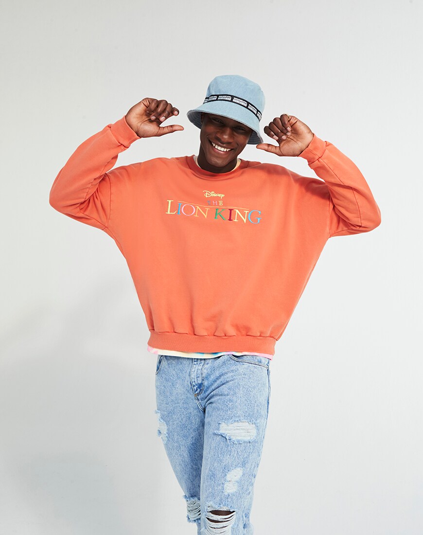 A picture of a model wearing an orange sweatshirt from The Lion King X ASOS DESIGN collaboration. Available at ASOS.