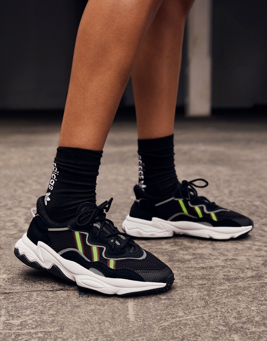 A picture of a model wearing a pair of black adidas Ozweego trainers.