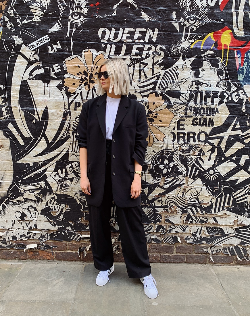 A picture of ASOS Insider, ASOS Kat wearing an oversized black blazer with black wide leg trousers and a pair of white and black adidas Superstar trainers.