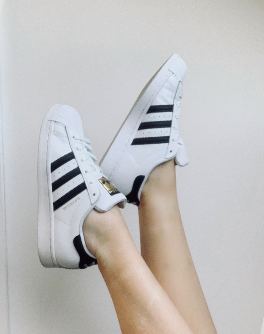 A picture of a pair of white adidas Superstar trainers with black 3-Stripe branding.
