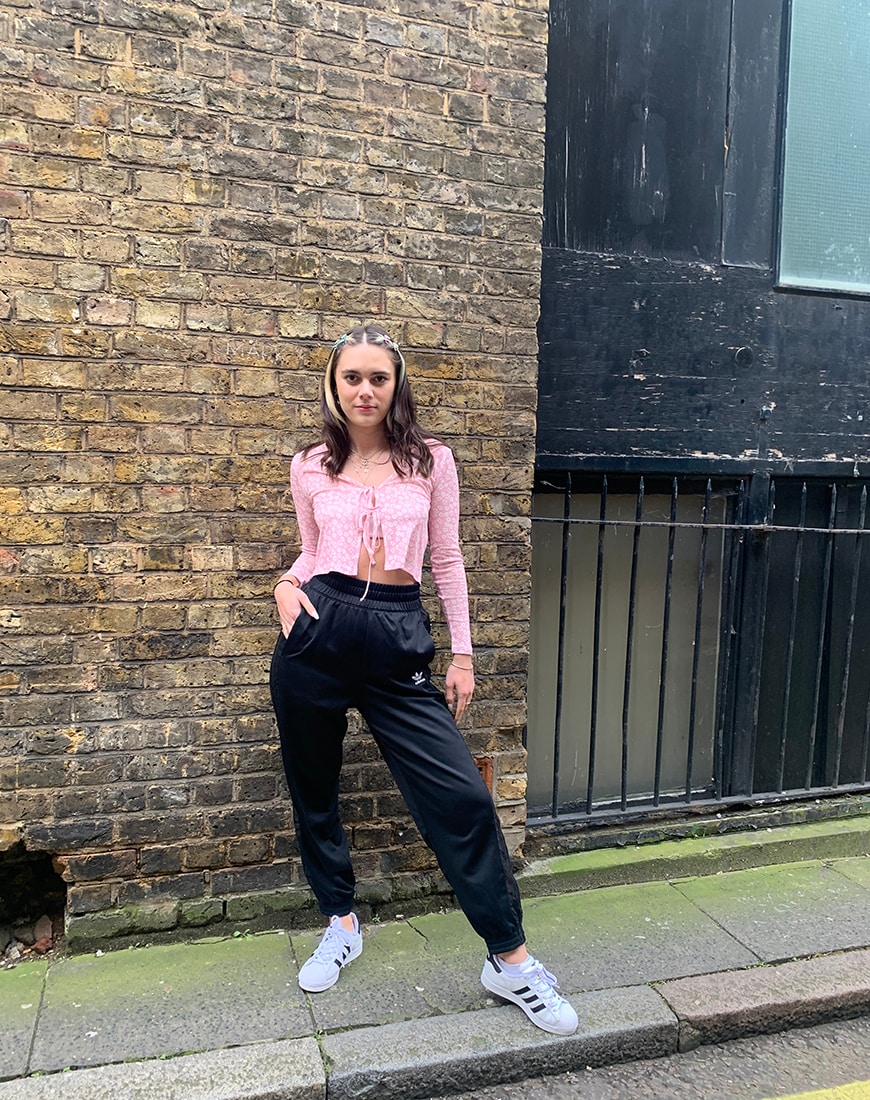 A picture of ASOS Insider, ASOS Olive wearing a daisy print crop top with black adidas tracksuit bottoms and adidas Superstar trainers.