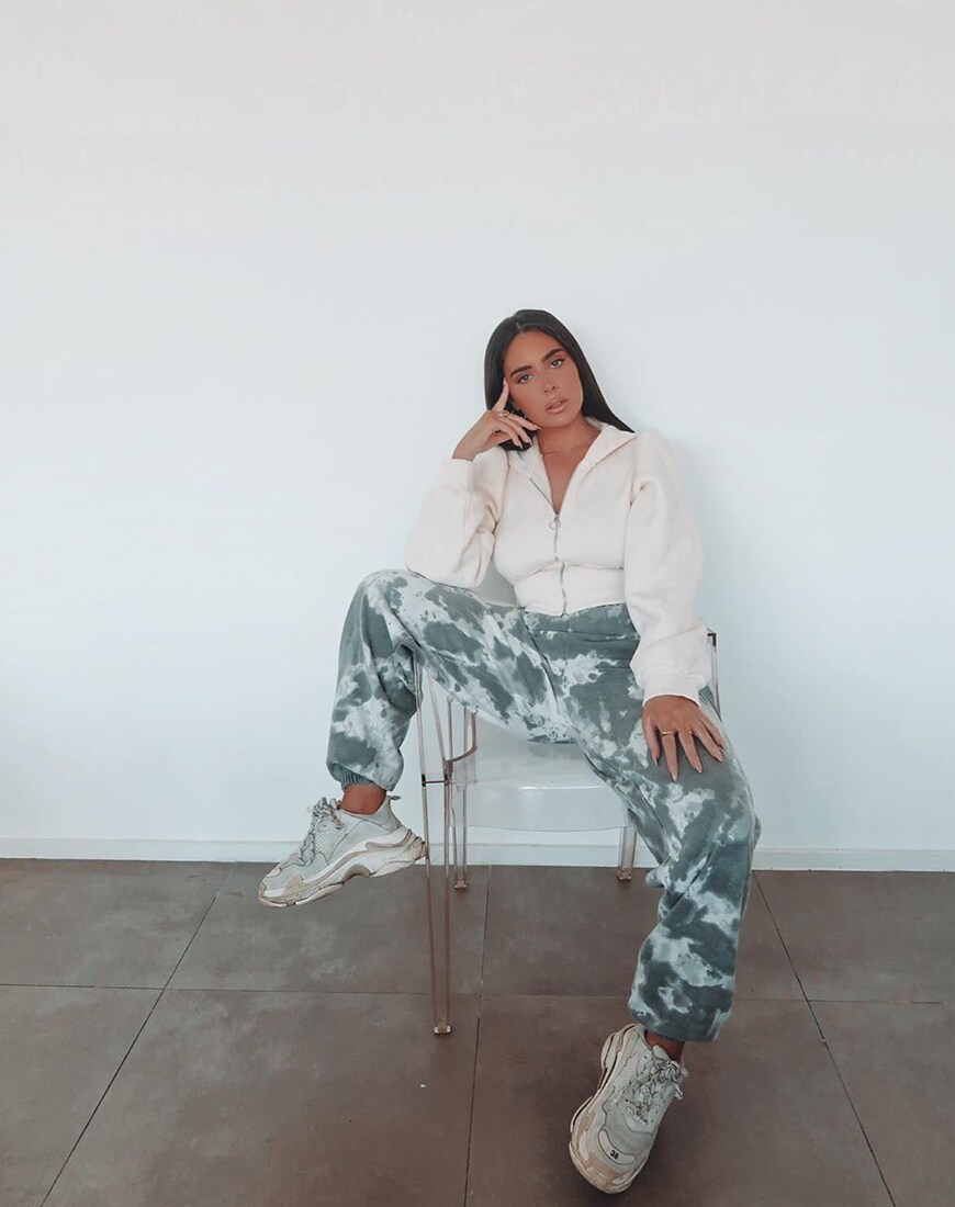 A picture of a woman wearing tie-dye joggers, chunky trainers, and a zip-up top.