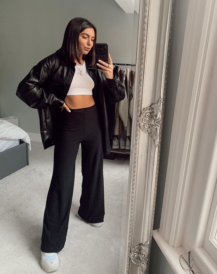 A picture of a woman wearing a leather-look jacket, a crop top and black, wide-leg trousers. 