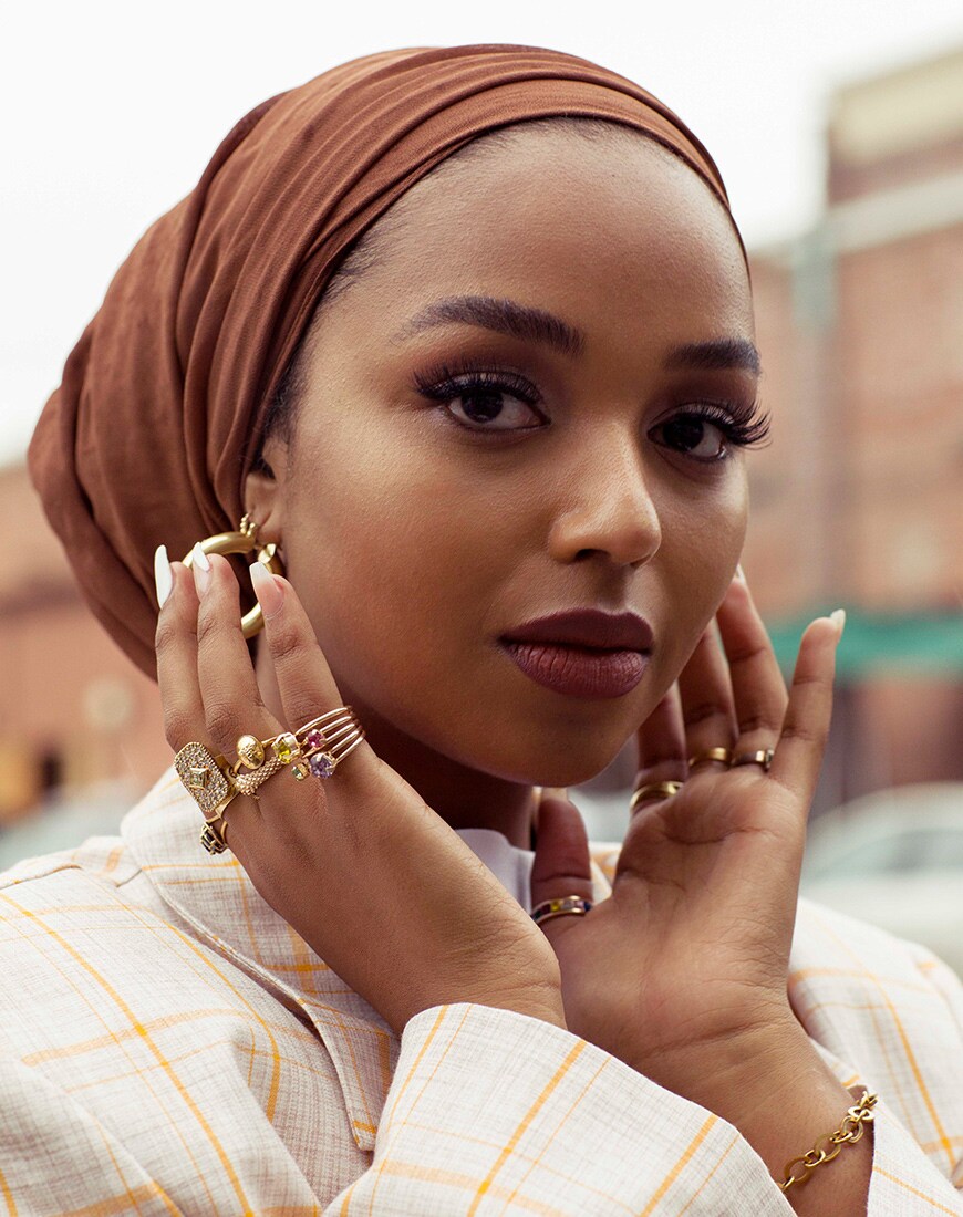 A picture of modest-fashion influencer and beauty blogger Shahd Batal wearing a hijab, stacked rings and a check blazer.