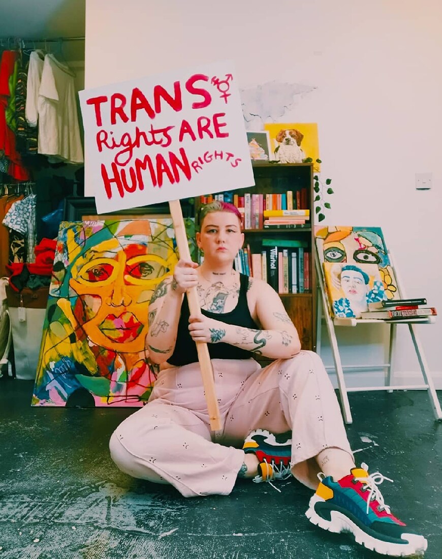 Wednesday Holmes holds a placard that says Trans Rights are Human Rights | ASOS Style Feed