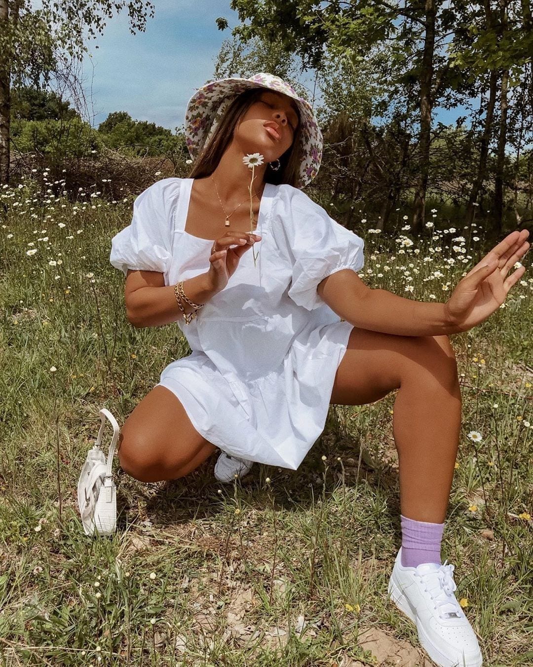 Sarah wears a white babydoll dress and floral bucket hat 