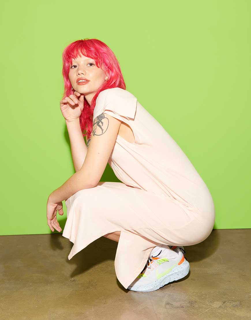Florence, a woman with red hair stands crouched in a cream dress and Nike Crater trainers | ASOS Style Feed