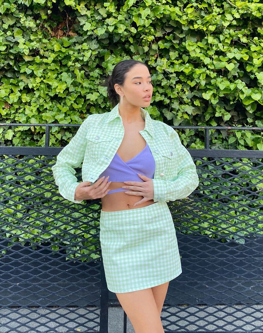 A woman wearing a green gingham jacket and skirt co-ord and purple crop top in front of a leaft background | ASOS Style Feed