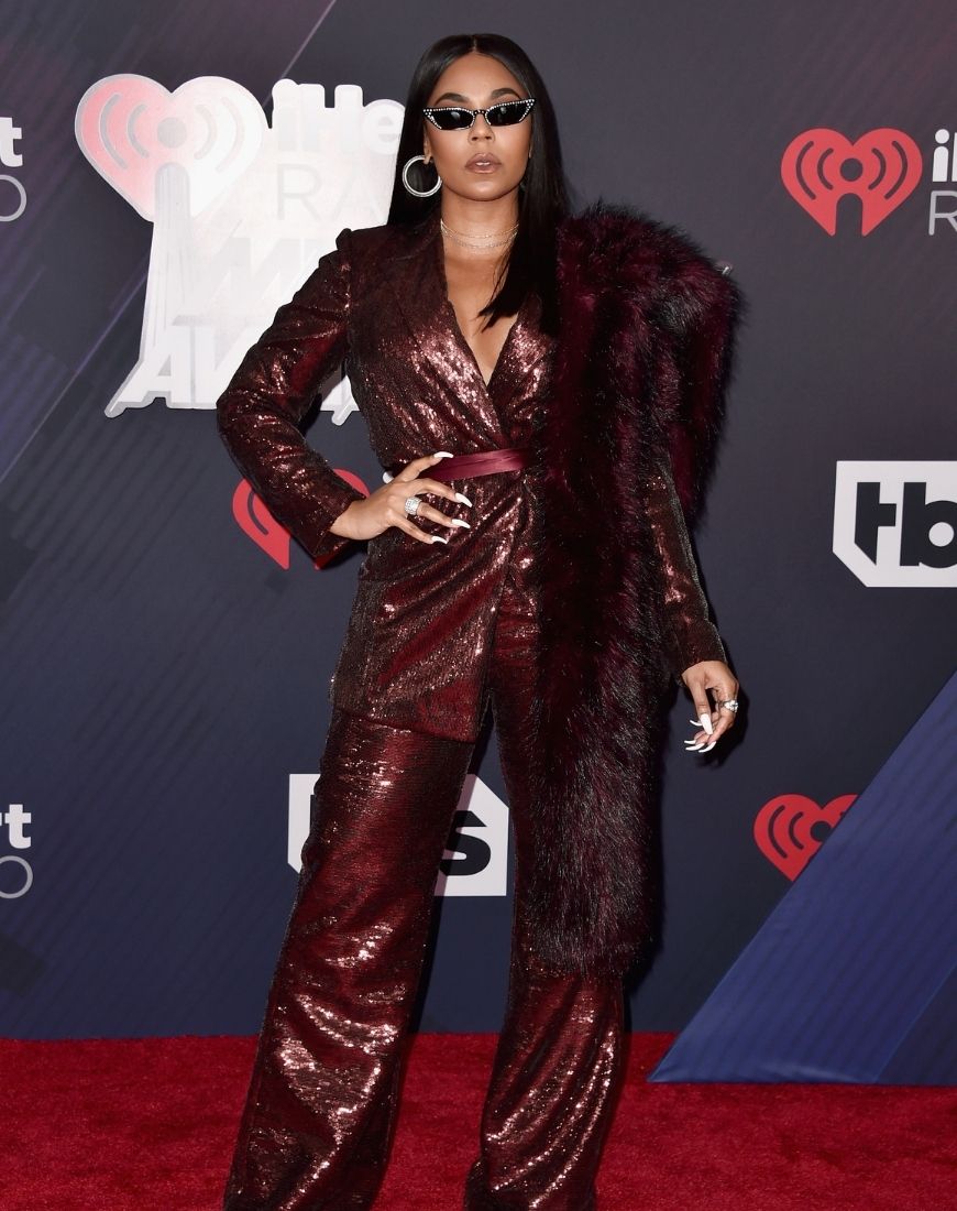 Ashanti poses in a sequinned crimson suit and a fur stole of the same colour. She's accessorised the look with a pair of sunglasses. | ASOS Style Feed