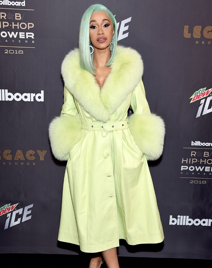 Cardi B wears a light green belted leather coat with fur sleeves and a fur neckline. Her hair is also green. | ASOS Style Feed
