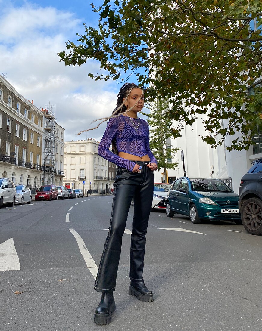 Charis stands on a road in a mesh purple long-sleeve top with a swirl print, black leather-look trousers and black chunky boots | ASOS Style Feed