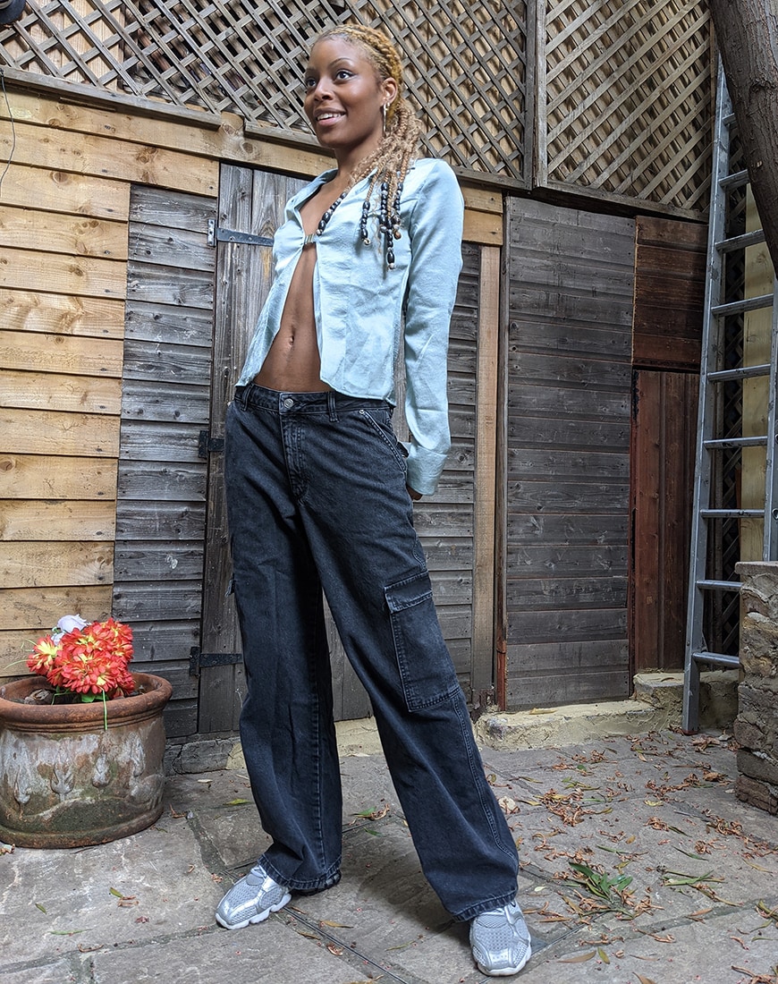 Marura stands in front of a fence in a baby blue blouse with an open front and single clasp, with black wide-leg jeans and trainers | ASOS Style Feed