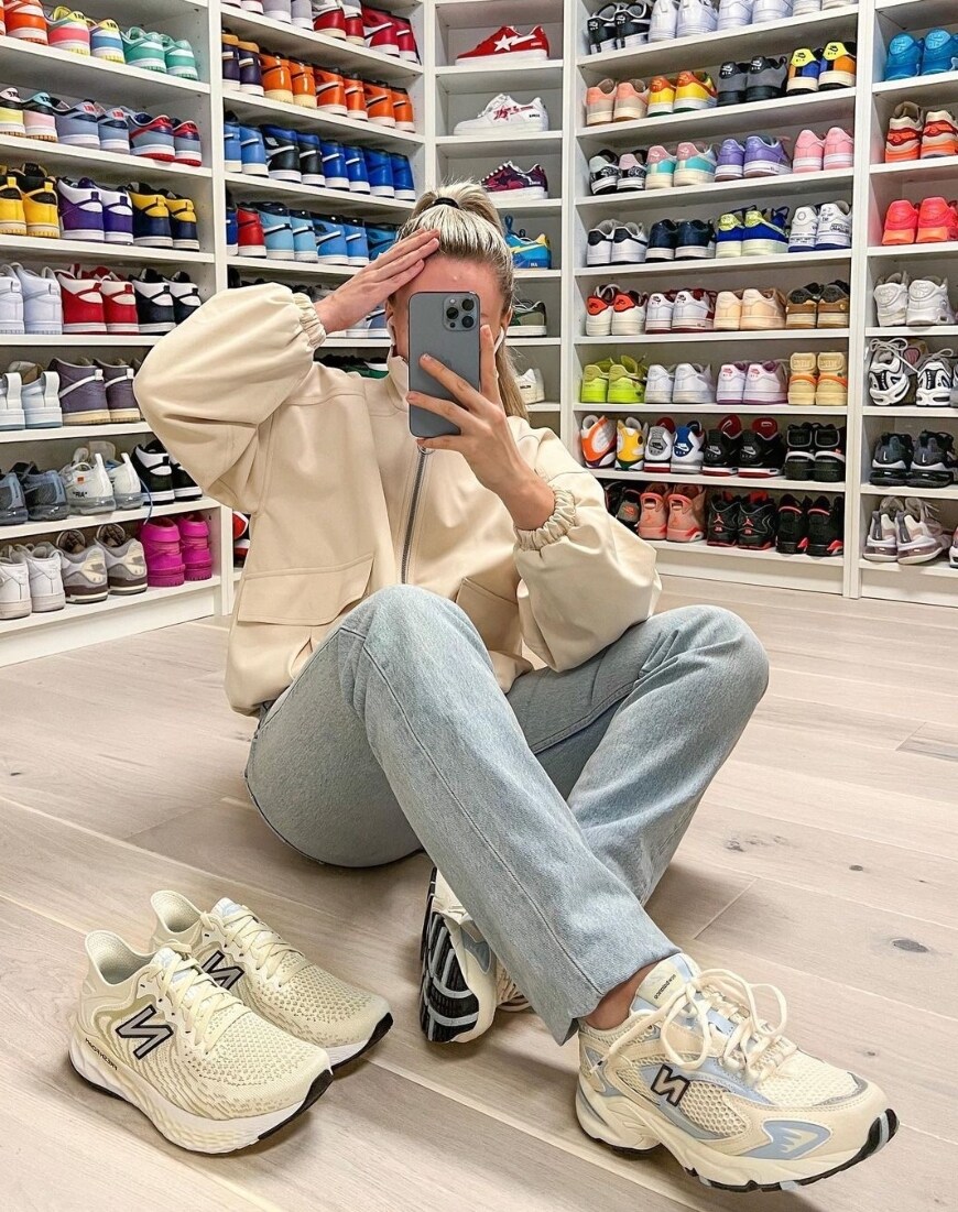 Woman sits in front of two walls of sneakers taking a mirror selfie in New Balance 725 trainers | ASOS Style Feed