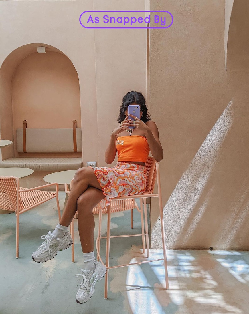 Woman wearing orange Ellesse top, swirl-print skirt and New Balance trainers | ASOS Style Feed