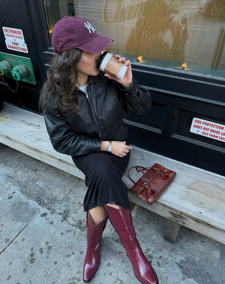 Woman drinking coffee in black outfit wearing red cowboy boots