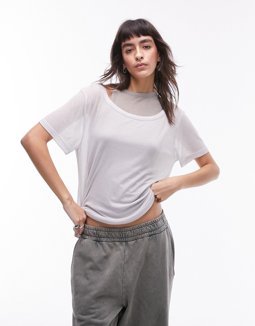 Woman wearing sheer white short sleeve on top of grey sleeveless vest top