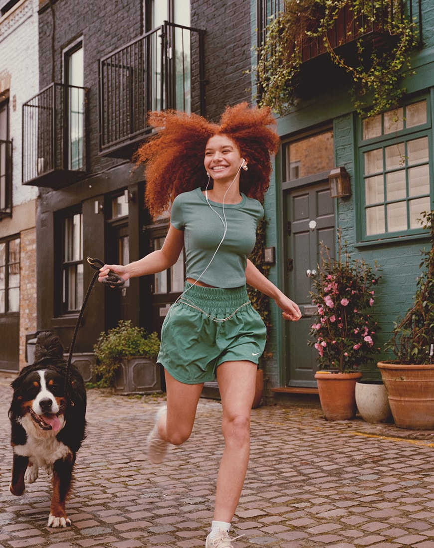 Woman wearing green Nike sportswear set and running with her dog