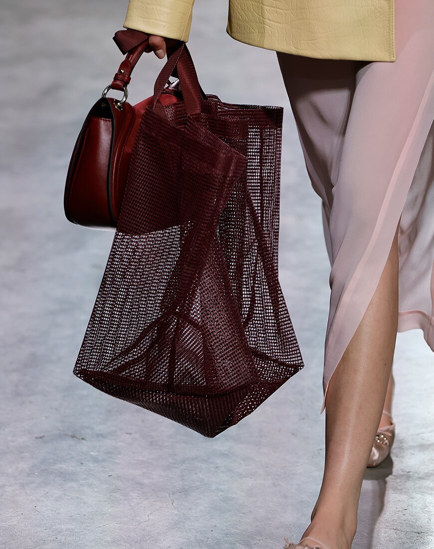 Woman holding deep red leather bag and deep red mesh bag