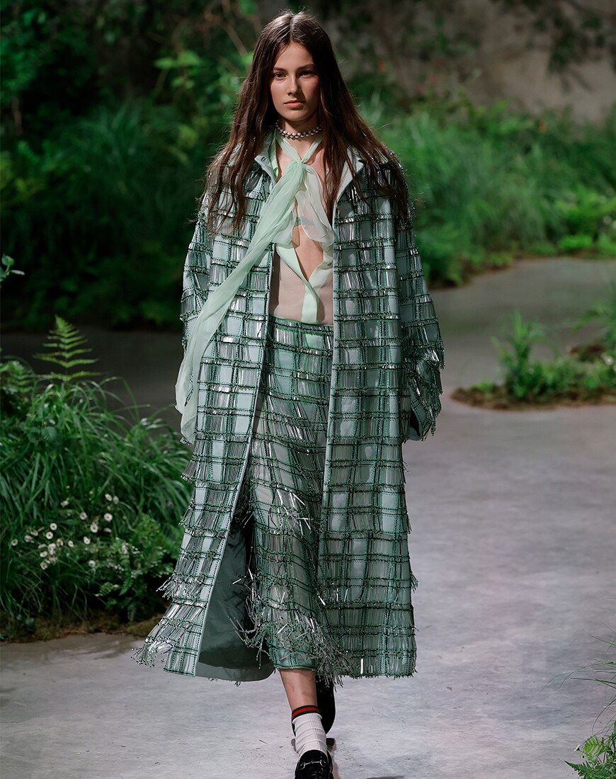 Model wearing green tartan outfit surrounded by greenery