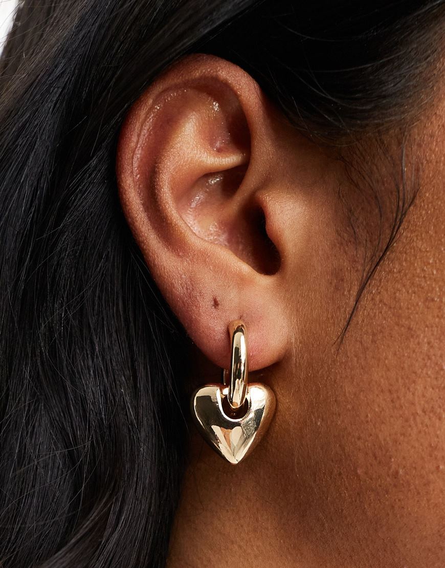 Person wearing  ASOS DESIGN hoop earrings with puff heart charm in gold tone