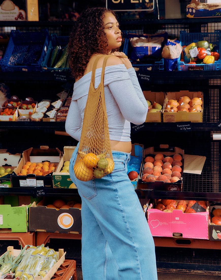 A woman wearing a grey off the shoulder top holding a bag of fruit | ASOS Style Feed