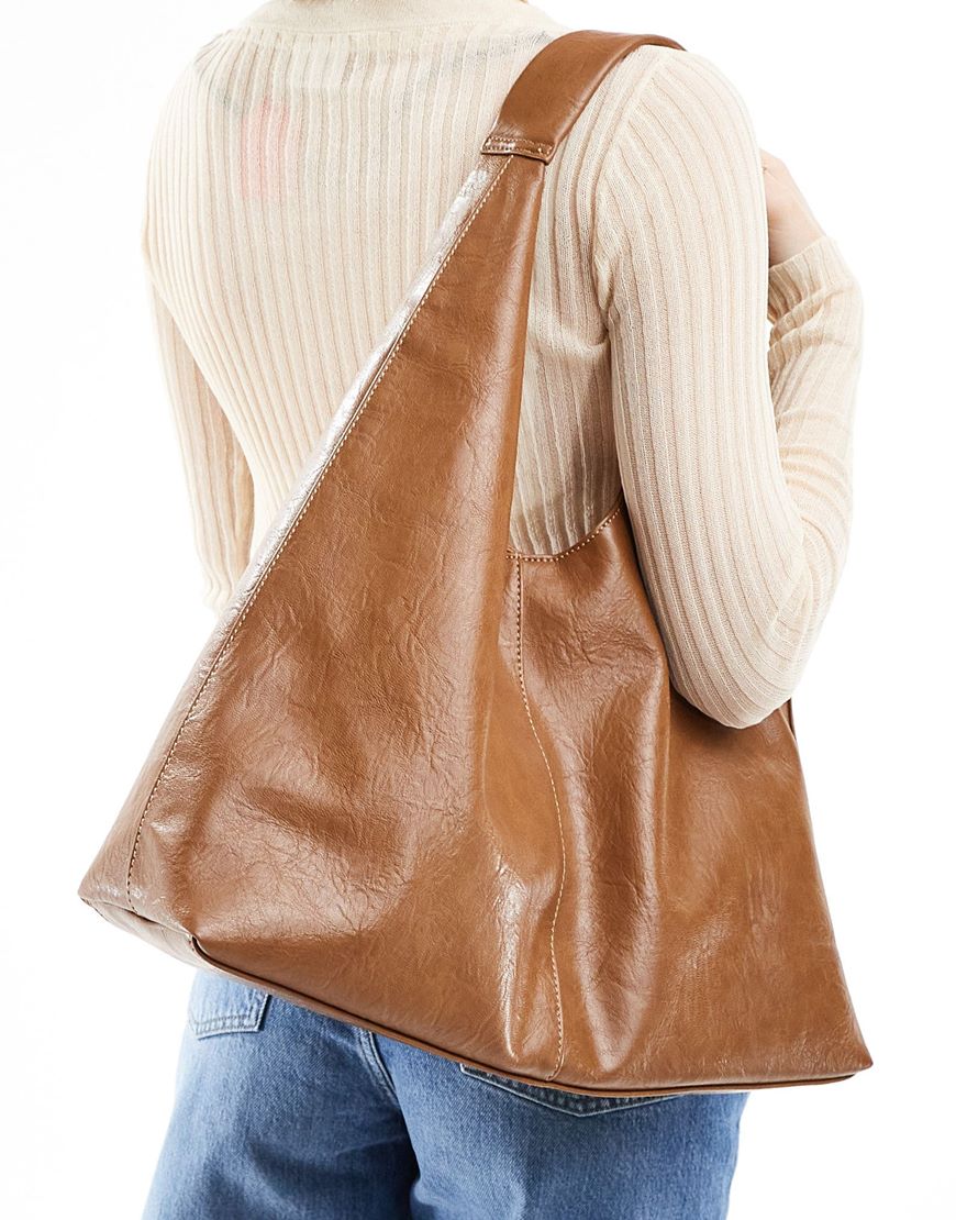 Woman holding tan triangular shaped shoulder bag