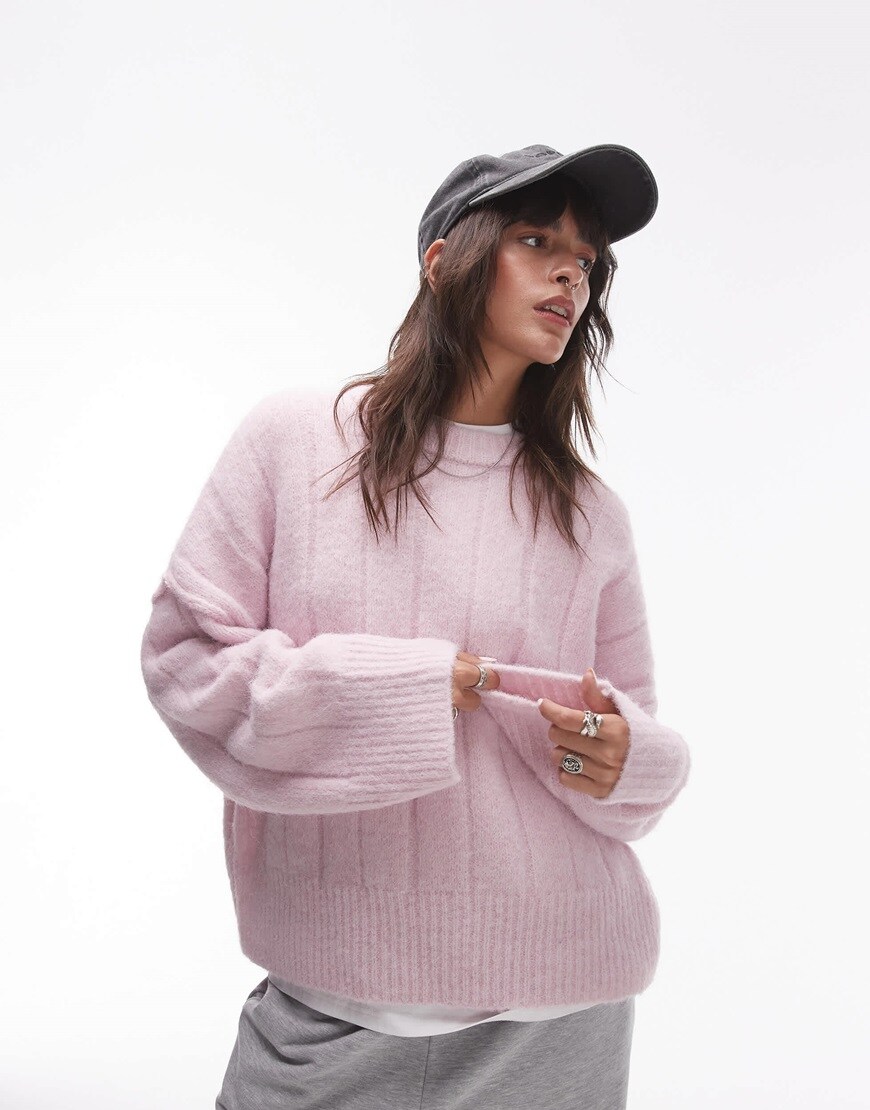 Model wearing black baseball cap with pastel pink long sleeve knitted jumper