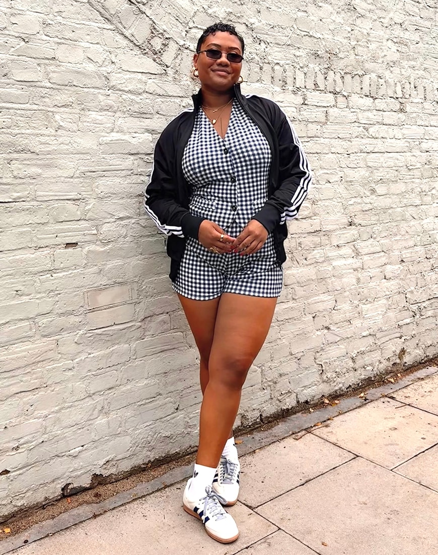Ebony-Renee Baker wearing checkered romper with black jacket and white and navy adidas Samba trainers