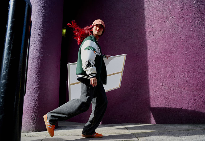 Model with red hair walking through streets holding a canvas