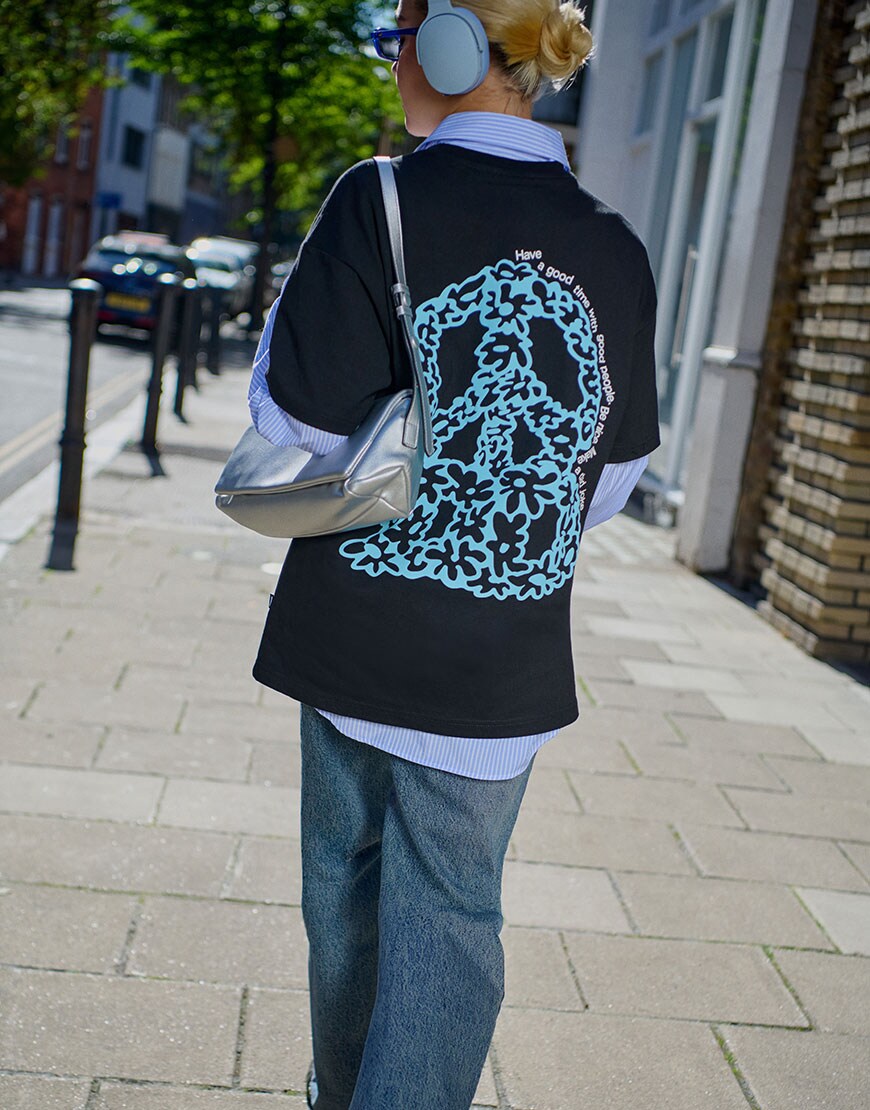 Model wearing black graphic tee with striped shirt and blue oversized jeans