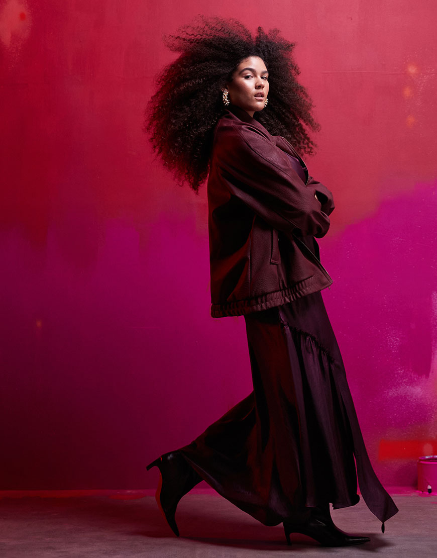 Model wearing sheer burgundy dress on a red background