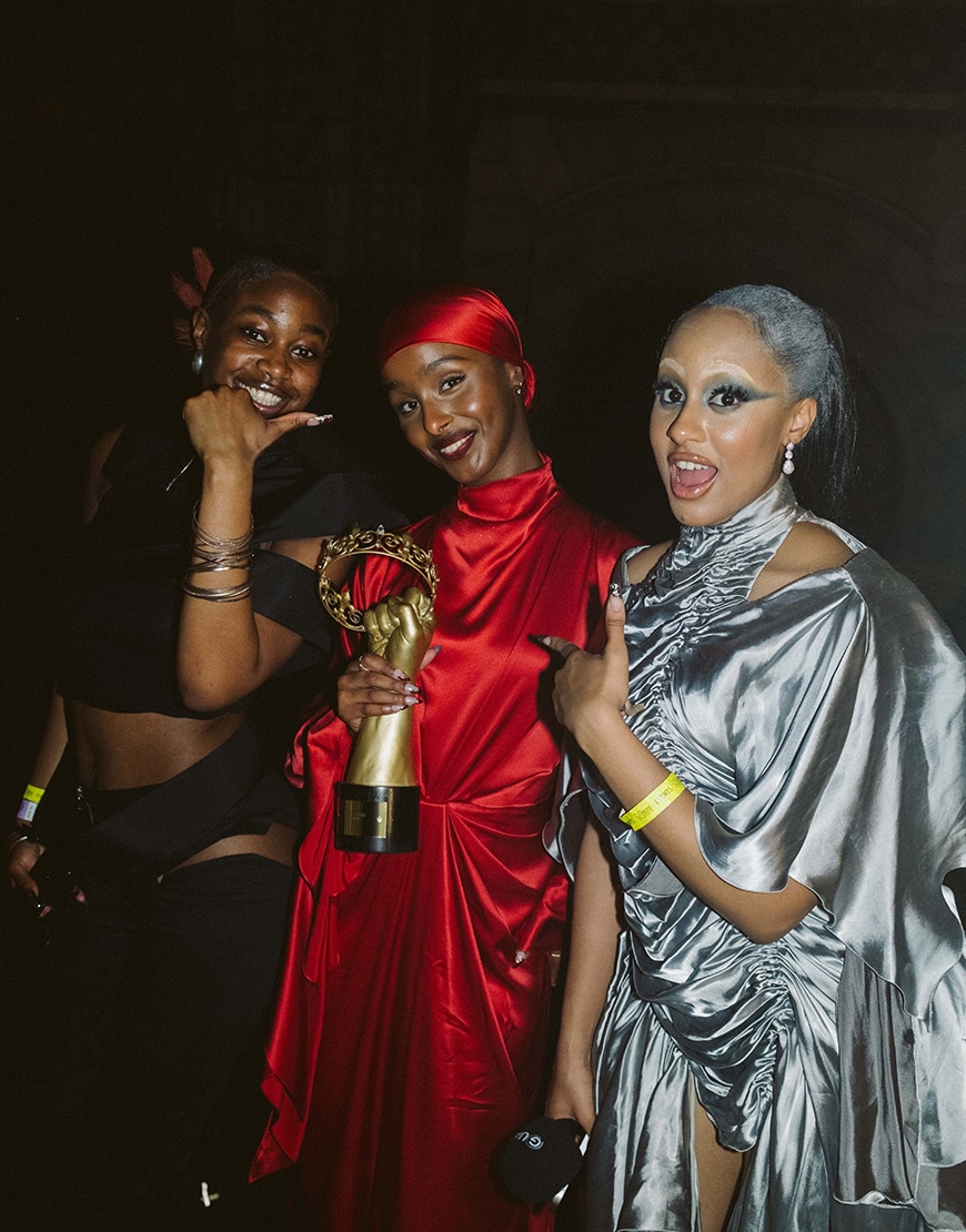 Three women with the middle woman holding a gold trophy